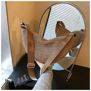 Detail of hand-held khaki woven straw moon bag with an adjustable wide brown shoulder strap