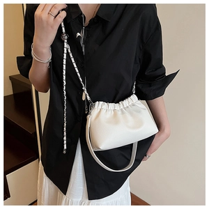 Détail d'un sac à main blanc plissé en cuir avec chaîne en métal porté par un mannequin