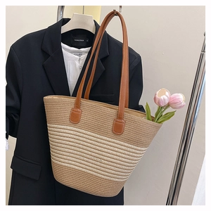 Gros plan d'un sac cabas en paille tissée avec anses en cuir brun sur un mannequin habillé