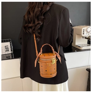 Detail of brown cylinder bucket bag with bear charm and silk scarf handle accent