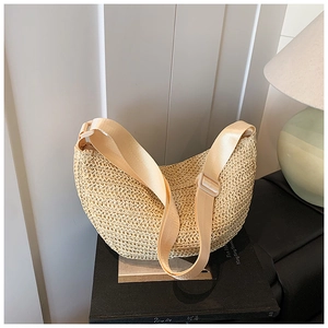 Macro detail of beige woven crescent bag with adjustable nylon strap on a dark book base