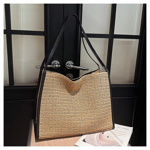 Détail d'un grand sac cabas en paille tressée avec anses en cuir noir contrastées