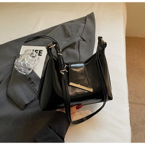 Detailansicht einer schwarzen Lackleder-Schultertasche mit eleganter Metallschnalle am Bett
