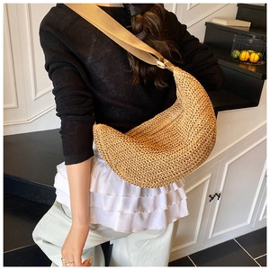 Detailed weave texture of a beige straw crescent bag with wide adjustable shoulder strap