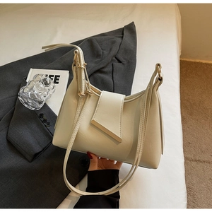 Detail einer cremeweißen Handtasche mit goldenen Metallbesatz auf einem grauen Blazer