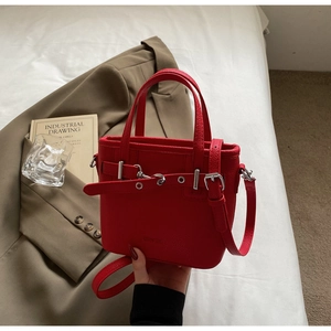 Dettaglio borsa tote in pelle rossa con fibbia argento e tracolla su lenzuola bianche