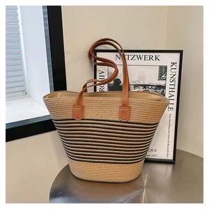 Détail d'un sac cabas en paille avec rayures noires et anses en cuir brun sur une table