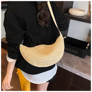 Detail of hand-woven beige half-moon straw bag with textured finish and shoulder strap