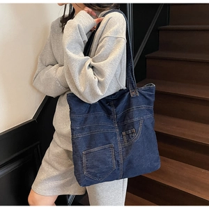Close-up of a blue denim tote bag with classic pocket details on casual grey sweatshirt