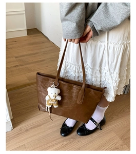 Close-up of coffee brown tote bag featuring crocodile pattern and a cute white bear charm