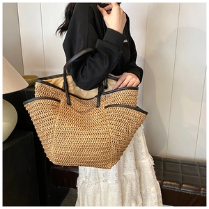 Detail of the large straw tote bag featuring black leather handles and beige inner lining