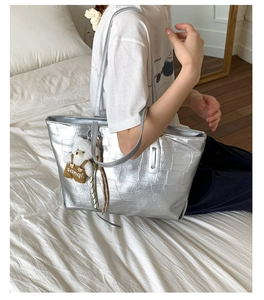 Silver crocodile texture tote bag with plush bear charm worn by a model on shoulder