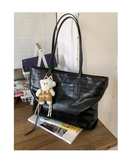 Detail view of black crocodile pattern tote bag with a cute plush bear pendant on wooden desk