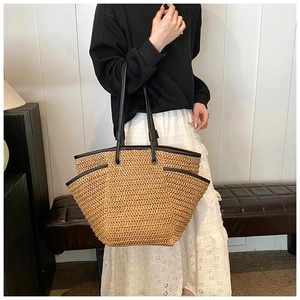 Detail of hand-woven straw tote bag with black leather handles and side pocket