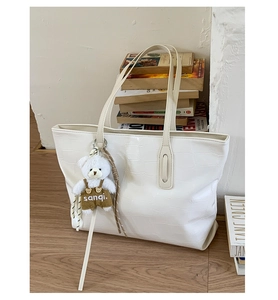 Close-up of white crocodile pattern tote bag with a cute bear charm and retro book background