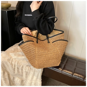 Detail of a large woven straw tote bag with black leather handles and interior lining