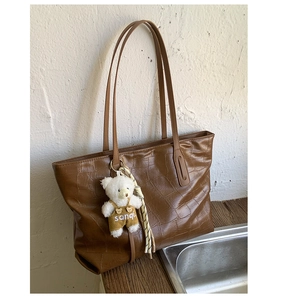 Detail of brown crocodile pattern tote bag with white teddy bear pendant accessory