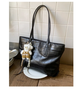 Detail of black crocodile texture tote bag with a cute plush bear pendant and thin straps