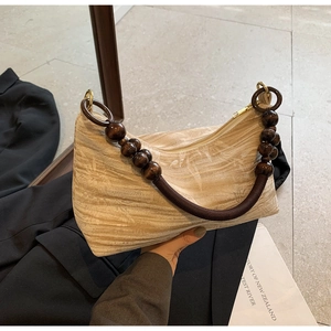 Detail of beaded wood handle on cream pleated handbag with golden hardware and zipper