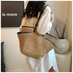 Minimalist woven straw tote bag with black leather straps worn by a model in a modern room