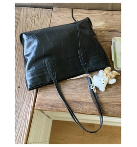 Detail of black faux leather tote with crocodile texture and cute bear pendant charm
