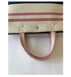 Detail of red checkered stripes on canvas tote with reinforced X-stitching and metal snap