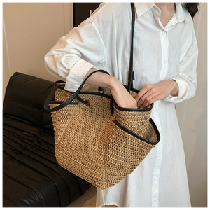 Detail of minimalist straw tote bag with black leather handles and front pocket on model