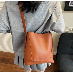 Close-up of caramel brown leather bucket bag with wide adjustable shoulder strap on model