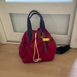 Close-up of red nylon backpack with yellow drawstring, fashion patch and brown dog charm