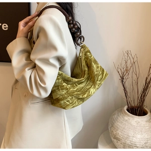 Detail of olive green velvet handbag featuring leaf patterns and wooden beaded handle