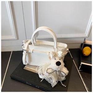 Détail d'un sac seau blanc avec breloque d'ours en peluche sur un support sombre