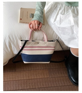 Detail view of the canvas tote bag showing contrast stripes and leather shoulder strap