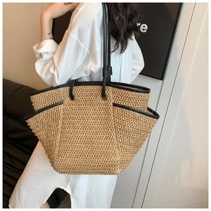 Detail of minimalist straw tote bag with black leather trim and long shoulder straps