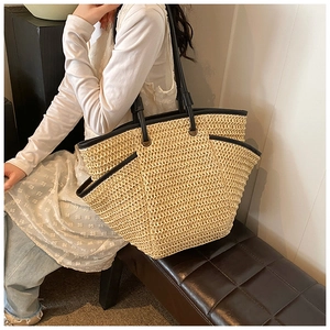Detailed texture of handwoven straw tote bag with black trim on a leather bench