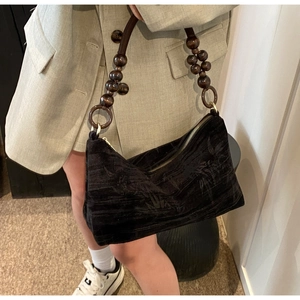 Detail of black woven shoulder bag with floral pattern and wooden bead strap handle