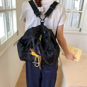 Detail view of black nylon drawstring backpack with cute plush dog pendant and versatile straps
