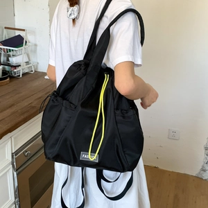 Detail of black drawstring backpack with fashion label and yellow contrast cord on model