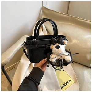 Gros plan d'un sac cabas noir brillant avec pendentif chiot en peluche sur un canapé