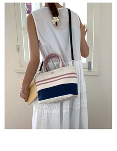 Detail of striped canvas tote bag with adjustable shoulder strap worn by a female model
