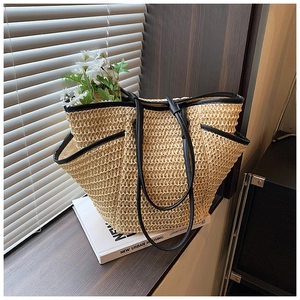 Close-up of minimalist woven straw tote bag with black leather trim and side pocket detail