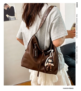 Detail view of large brown leather hobo bag featuring wide strap and cute doll charm
