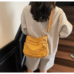 Detail of mustard yellow canvas crossbody bag with multiple zippers shown on a shoulder