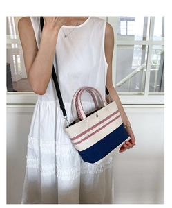 Detail of canvas tote bag with red stripes and navy bottom worn by a model in a white dress