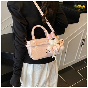 Sac seau en cuir verni rose avec charm de poupée en peluche porté par un mannequin