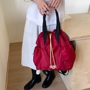 Detail of red nylon drawstring backpack featuring yellow cords and 'FASHION' label tag