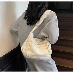 Detail of off-white canvas crossbody bag featuring functional zipper pockets and wide strap