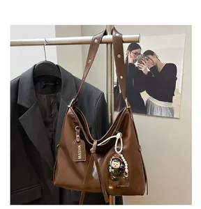 Detail view of brown leather tote bag with MASHK tag and cute girl doll pendant charm