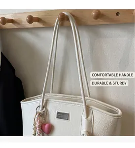 Detail of off-white wrinkled patent leather tote bag with silver plaque and heart charm