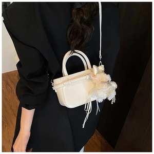 Détail du sac bandoulière en cuir verni blanc avec breloques fleurs en dentelle et nœud