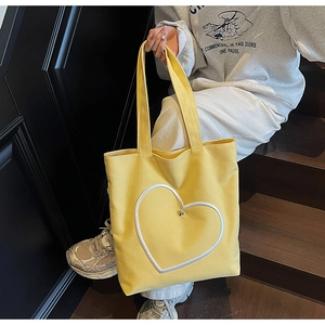 Détail d'un cabas en toile jaune avec broderie cœur blanche et perle métallique argentée